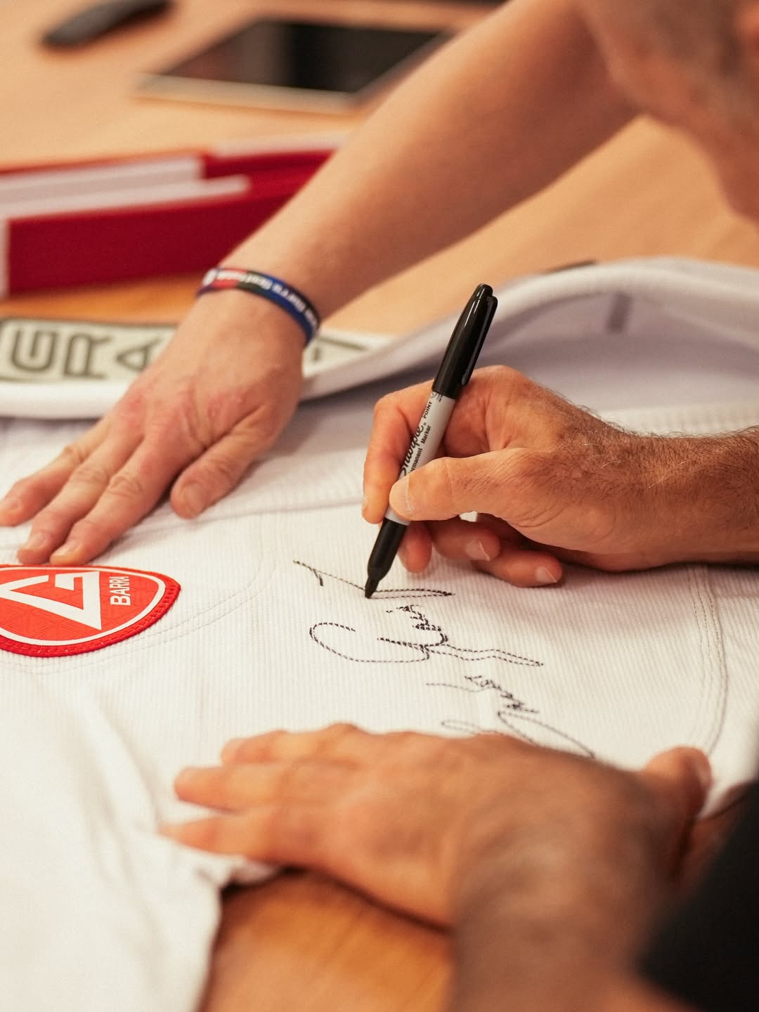 Detalhe das mãos de Carlos Gracie Jr. autografando um kimono da Gracie Barra