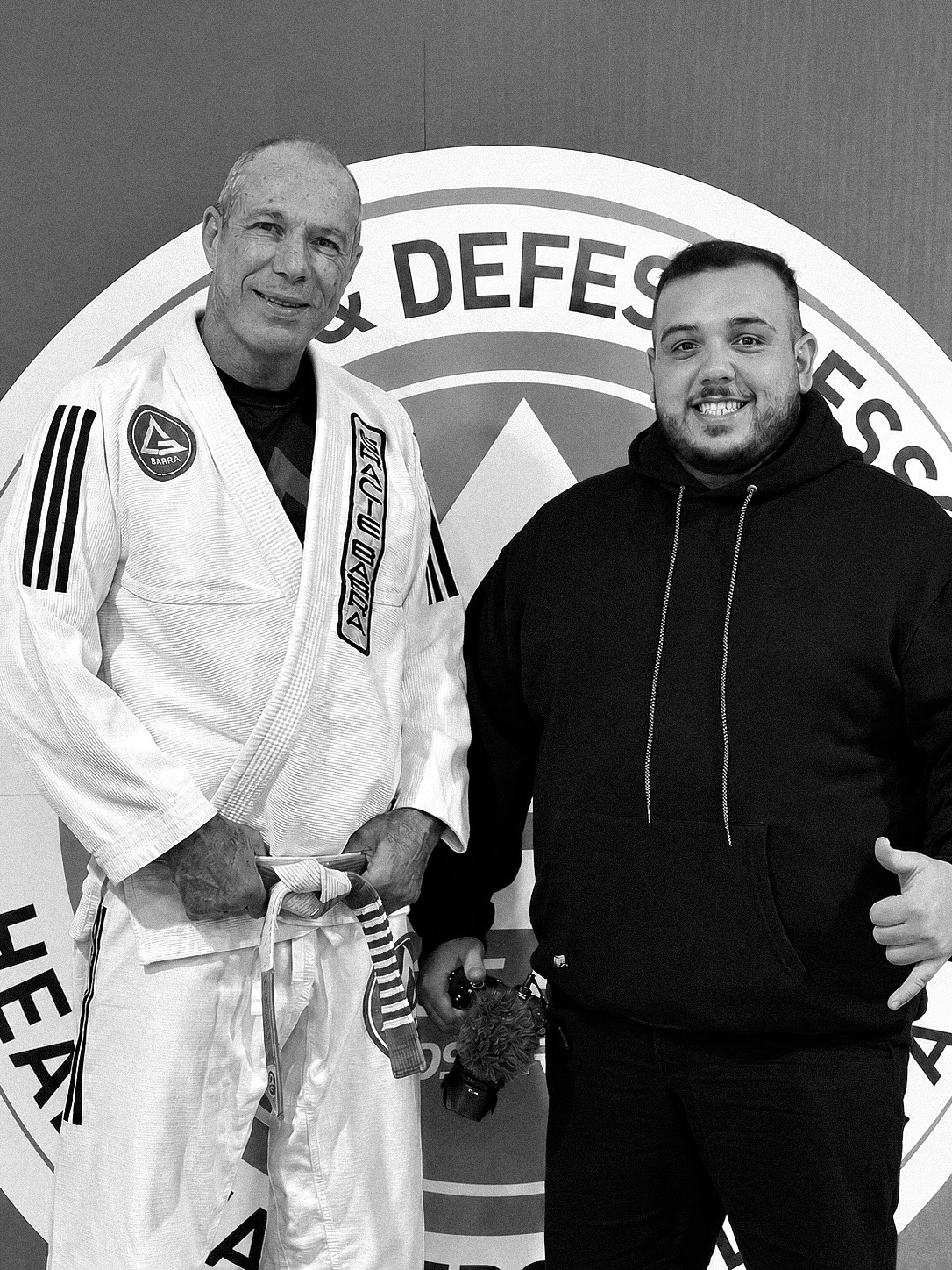 Em preto e branco, Carlos Gracie Jr., de kimono, ao lado de Vitor Freitas em um seminário em Florianópolis, em 2022