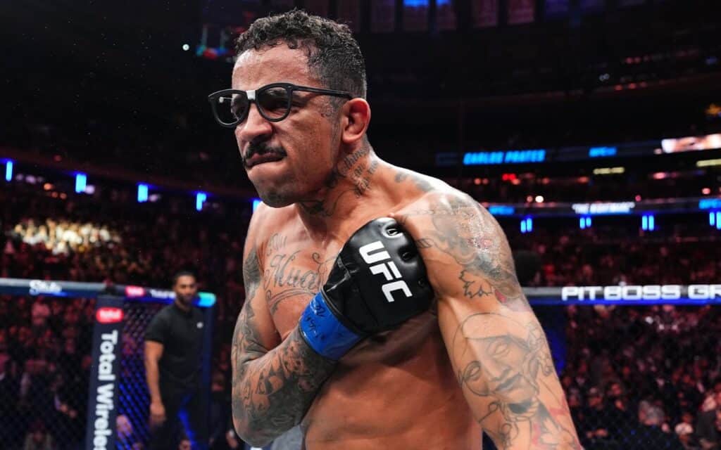 Carlos Prates de óculos escuros e luva no peito no octógono do UFC 322