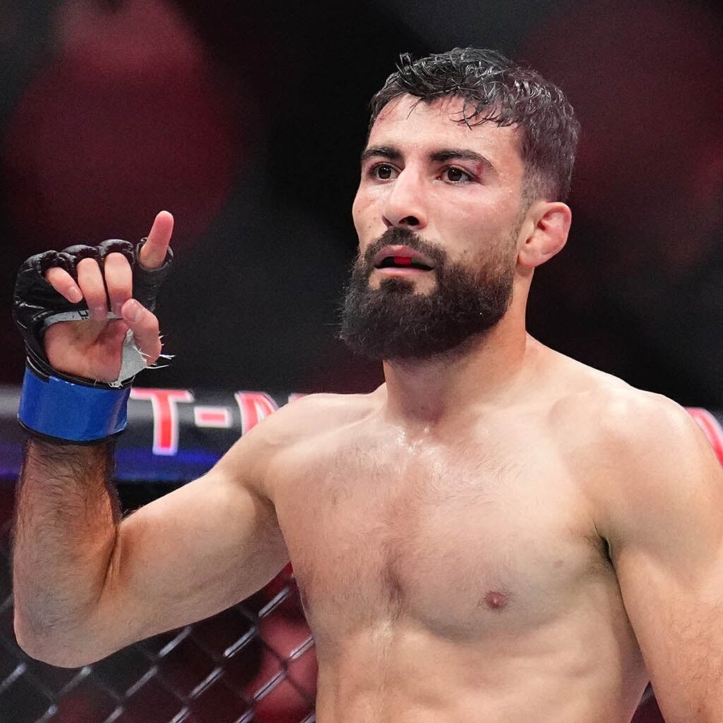 Muhammad Mokaev culpa TKO e Paramount por saída de Basharat 1 Farid Basharat de luvas azuis ergue a mão no octógono do UFC 320, em Las Vegas