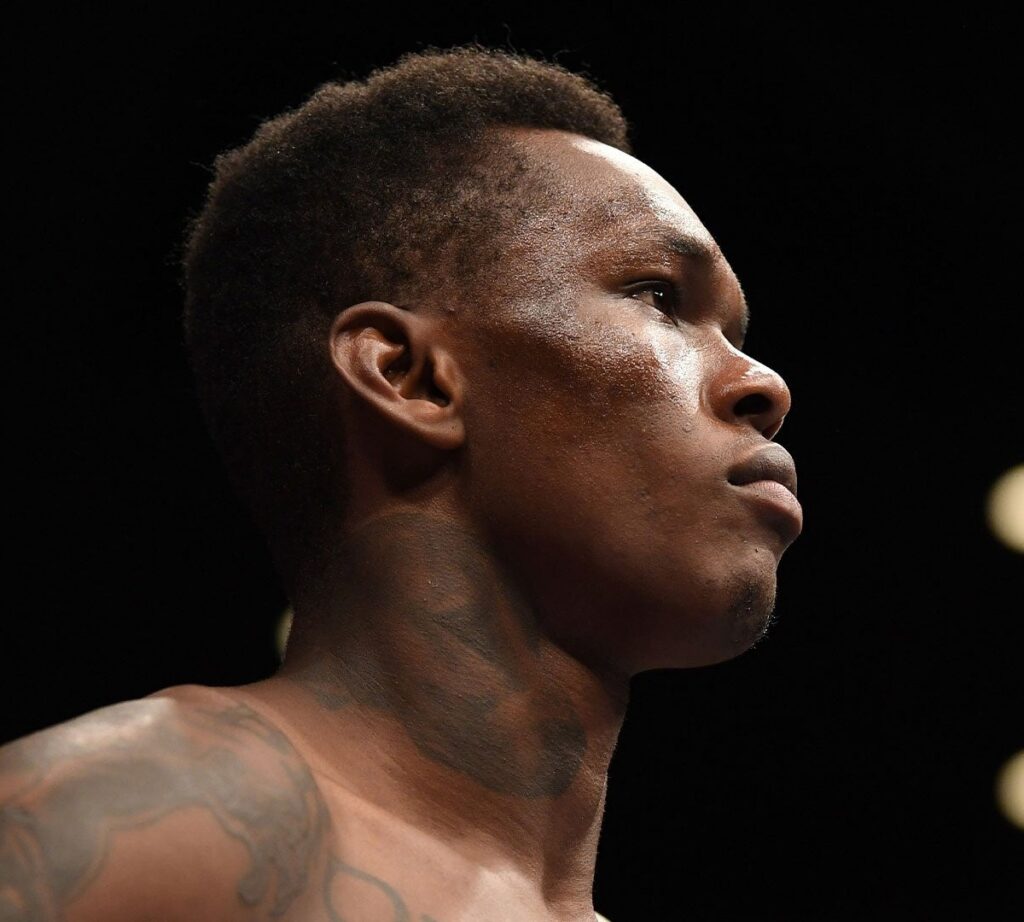 Israel Adesanya de perfil, sem camisa, no octógono antes da luta principal do UFC 234