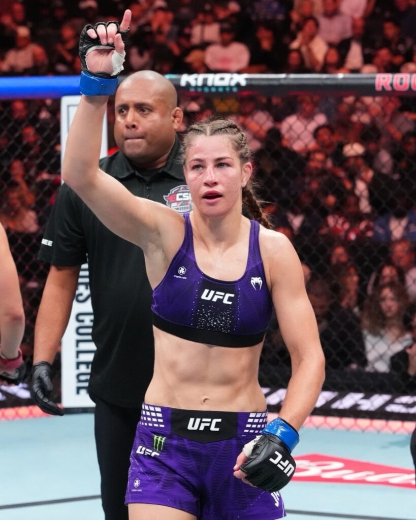 Jasmine Jasudavicius de top roxo ergue o punho no octógono após vencer Erin Blanchfield no UFC Edmonton