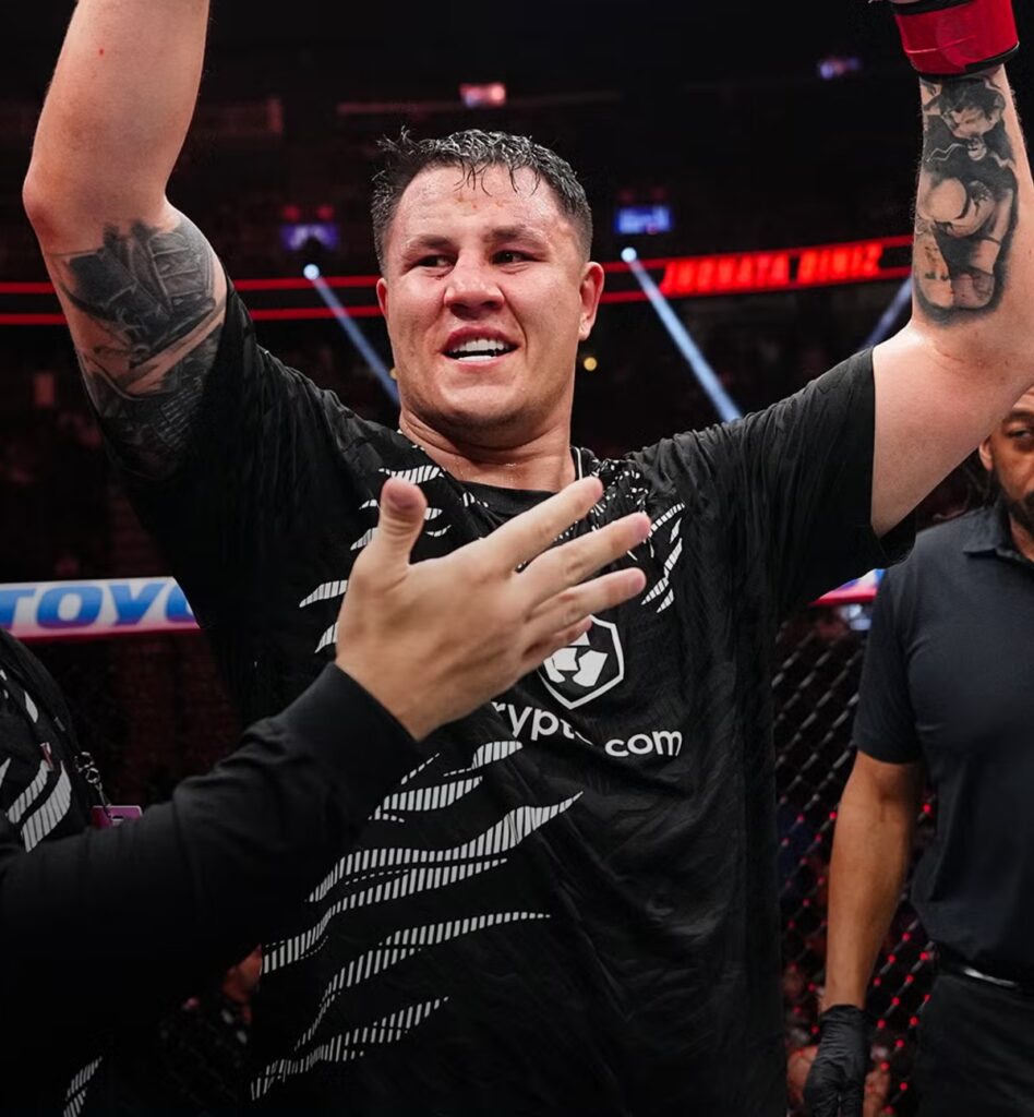 Jhonata Diniz de camiseta preta com os braços erguidos no Octógono após vencer Alvin Hines no UFC 317