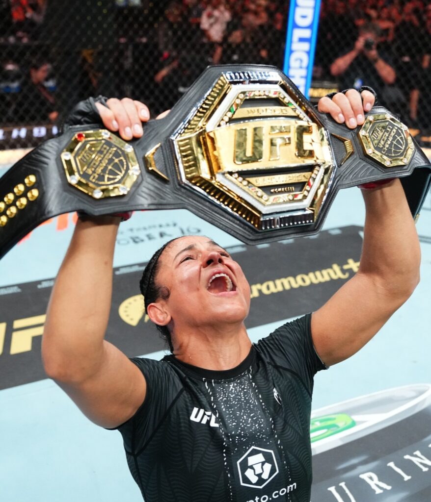 Natália Silva ergue o cinturão peso-mosca do UFC no octógono após vencer Wang Cong no UFC 332, em Salt Lake City