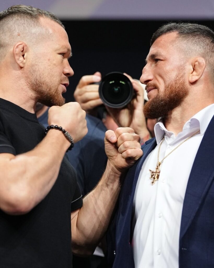 Petr Yan, de camiseta preta, e Merab Dvalishvili, de terno, frente a frente em encarada do UFC