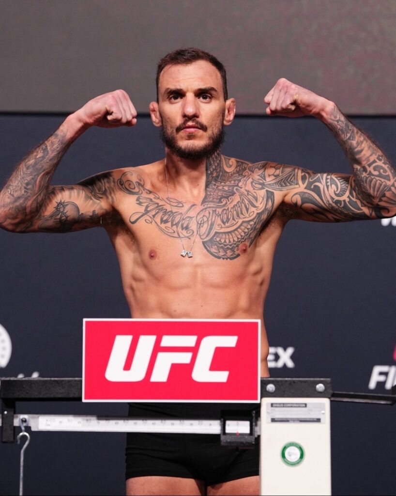Renato Moicano flexiona os braços sobre a balança na pesagem oficial do UFC Vegas 123, em Las Vegas