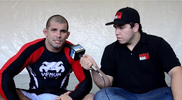 Vitor Freitas, de boné e camisa da GRACIEMAG, entrevista Rodolfo Vieira com o microfone da revista