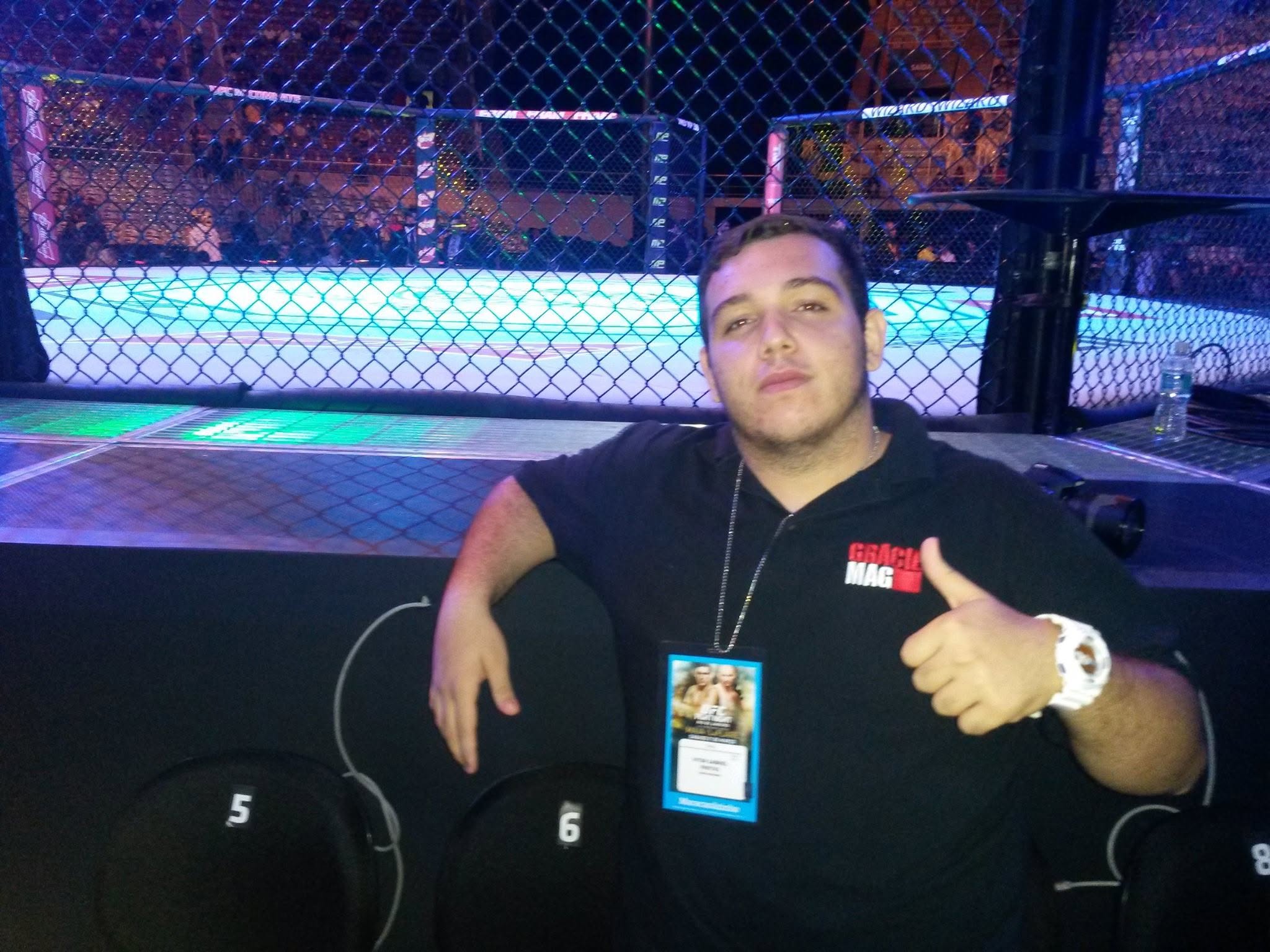 Vitor Freitas, com camisa da GRACIEMAG e credencial, ao lado do octógono do UFC, em 2015